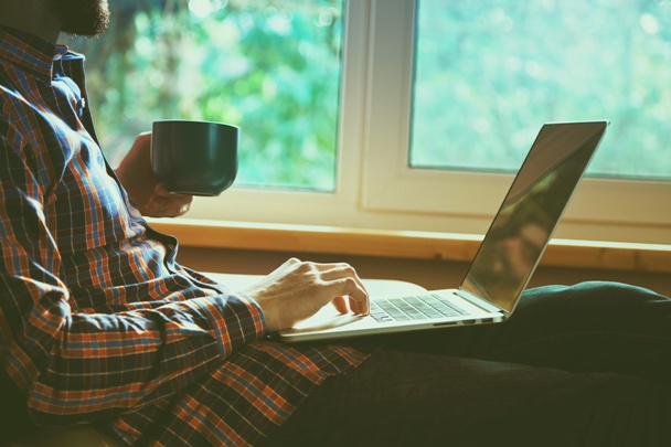 man lying with laptop drinking coffee or tea