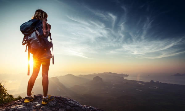 Lady hiker relaxing on top of hill and enjoying sunrise over the valley